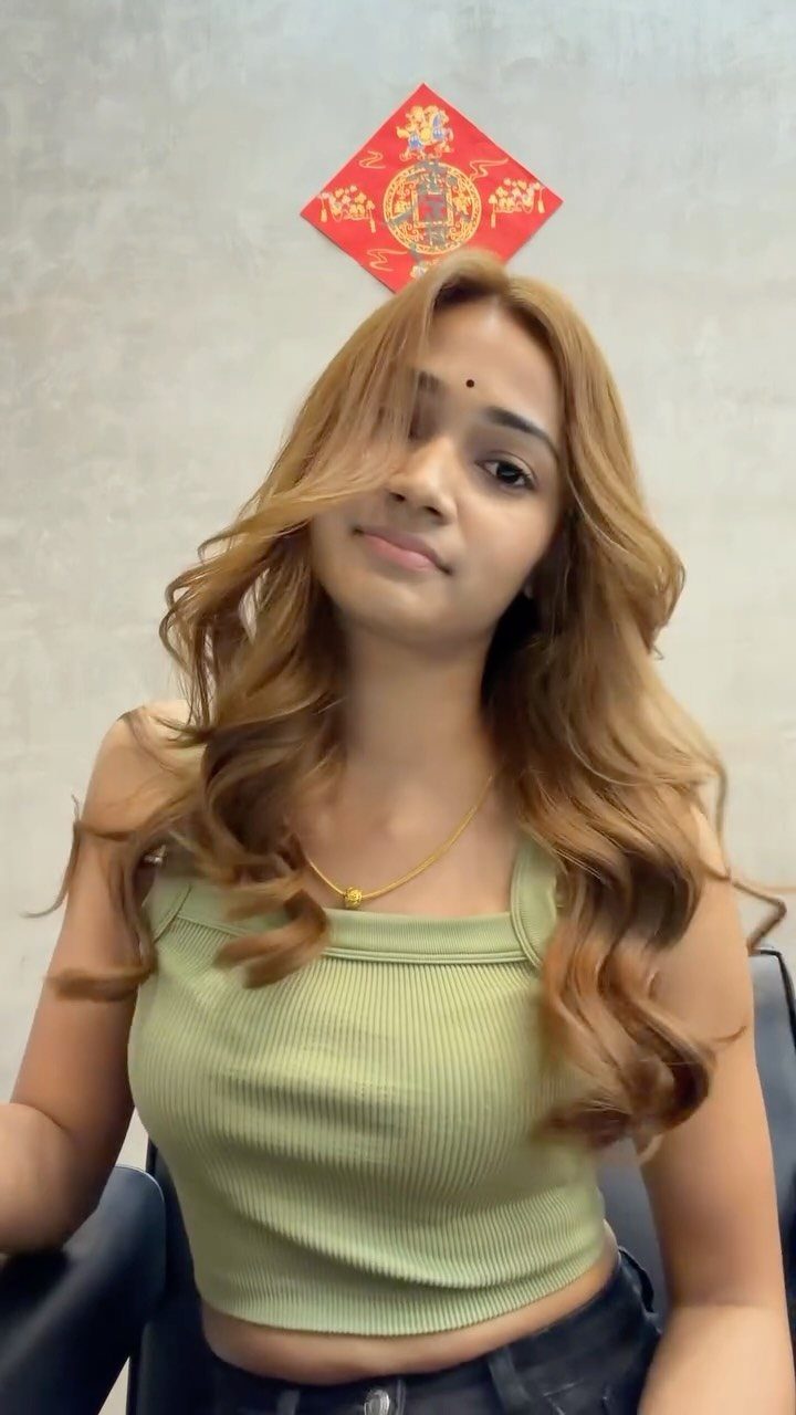Woman with long wavy brown hair and caramel face-framing highlights wearing green top.