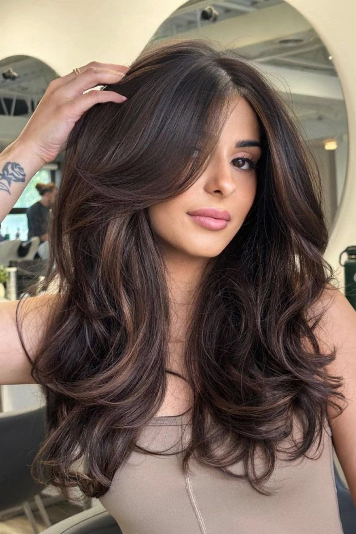 Woman with long wavy dark brown hair and chocolate brown face-framing highlights.