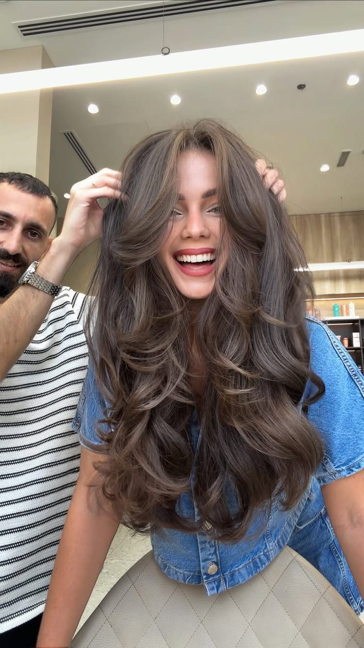 Woman with long layered brown hair and caramel highlights in a salon