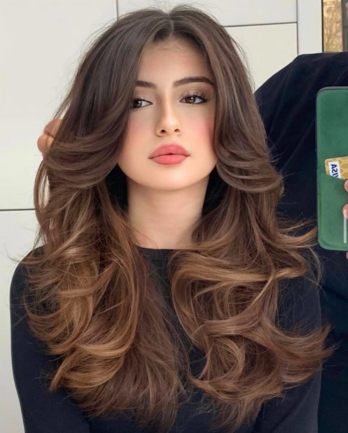 Woman with long wavy brown hair and caramel face-framing highlights posing for selfie