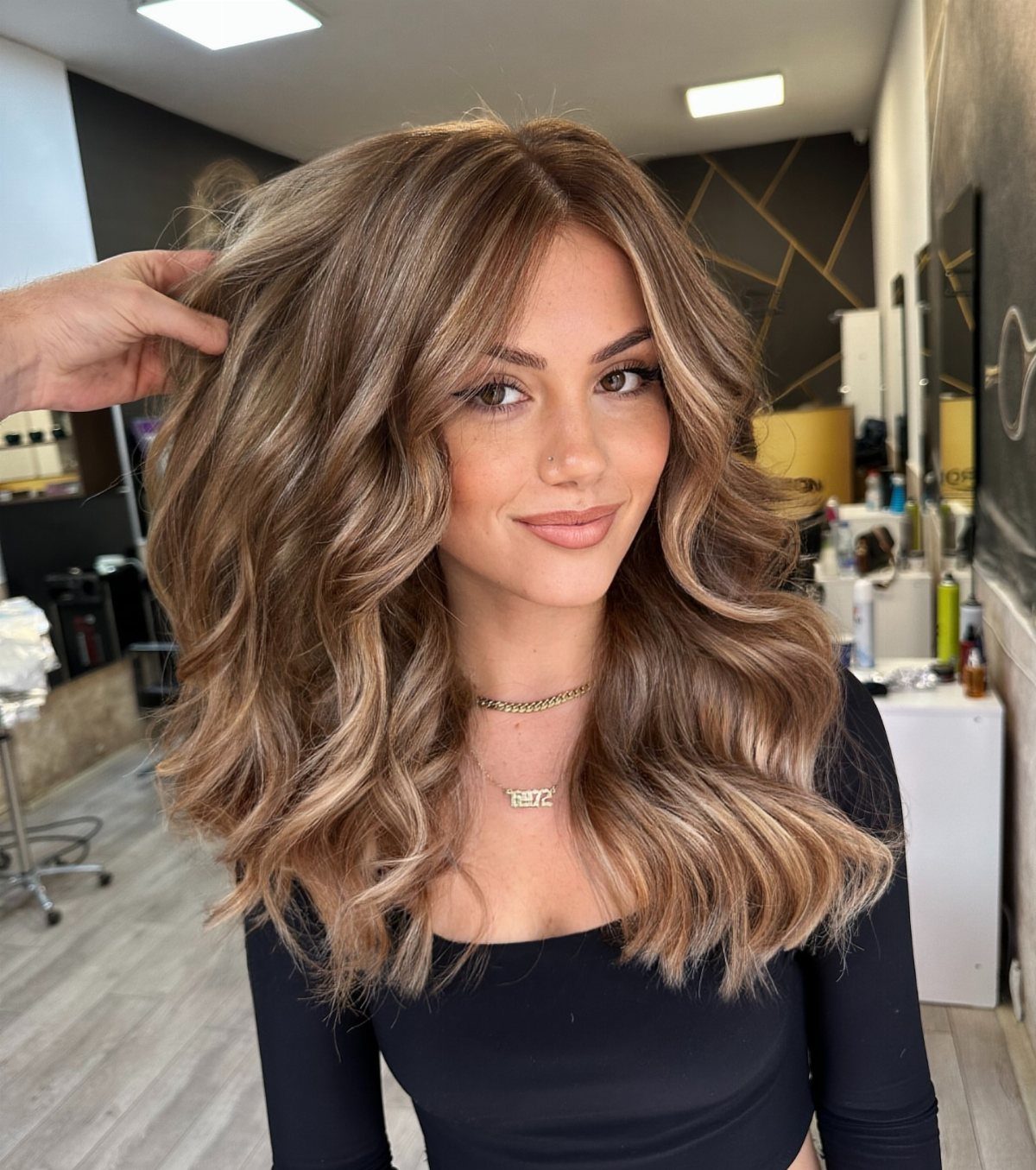 Woman with long wavy brown hair and softly blended caramel balayage highlights.