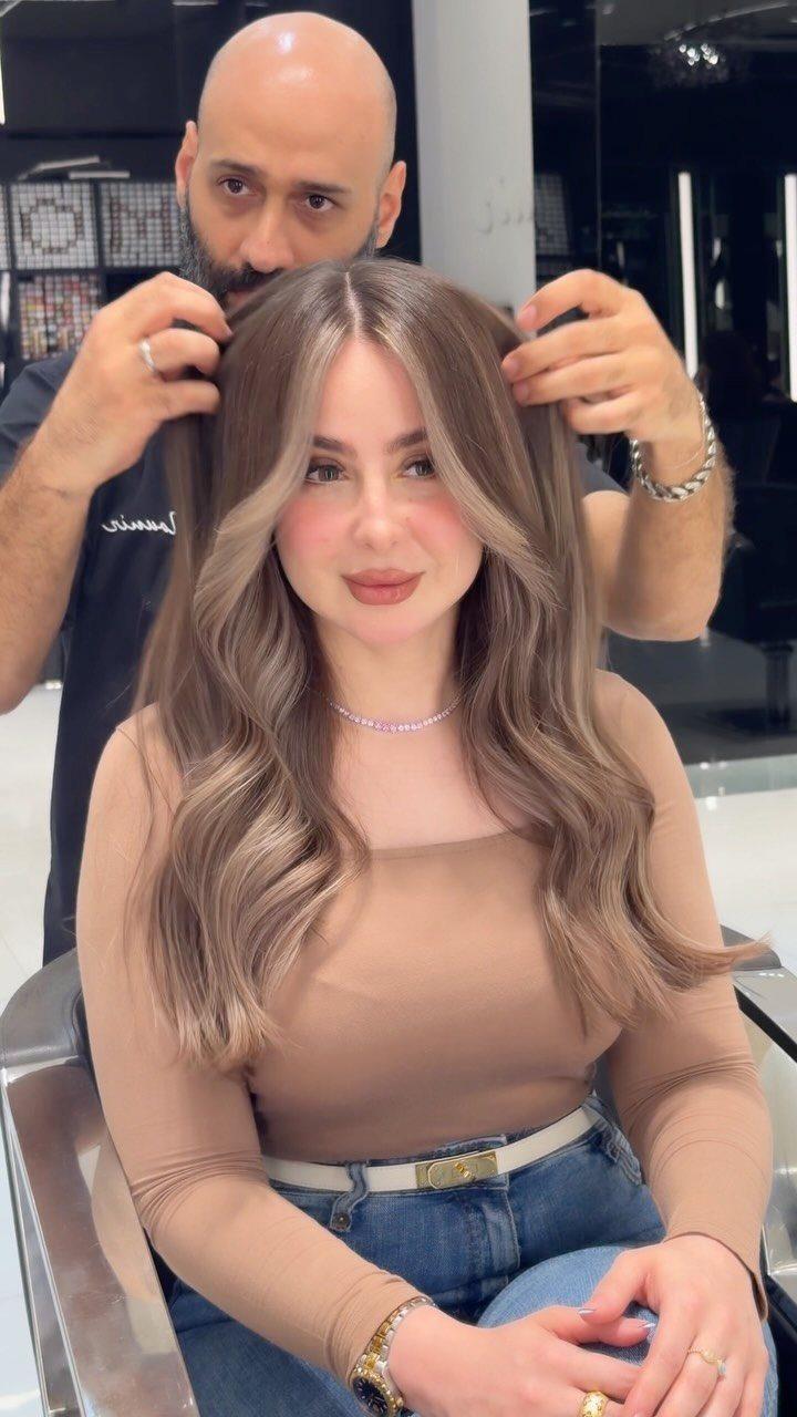 Woman with long wavy brown hair and champagne balayage highlights in a salon.