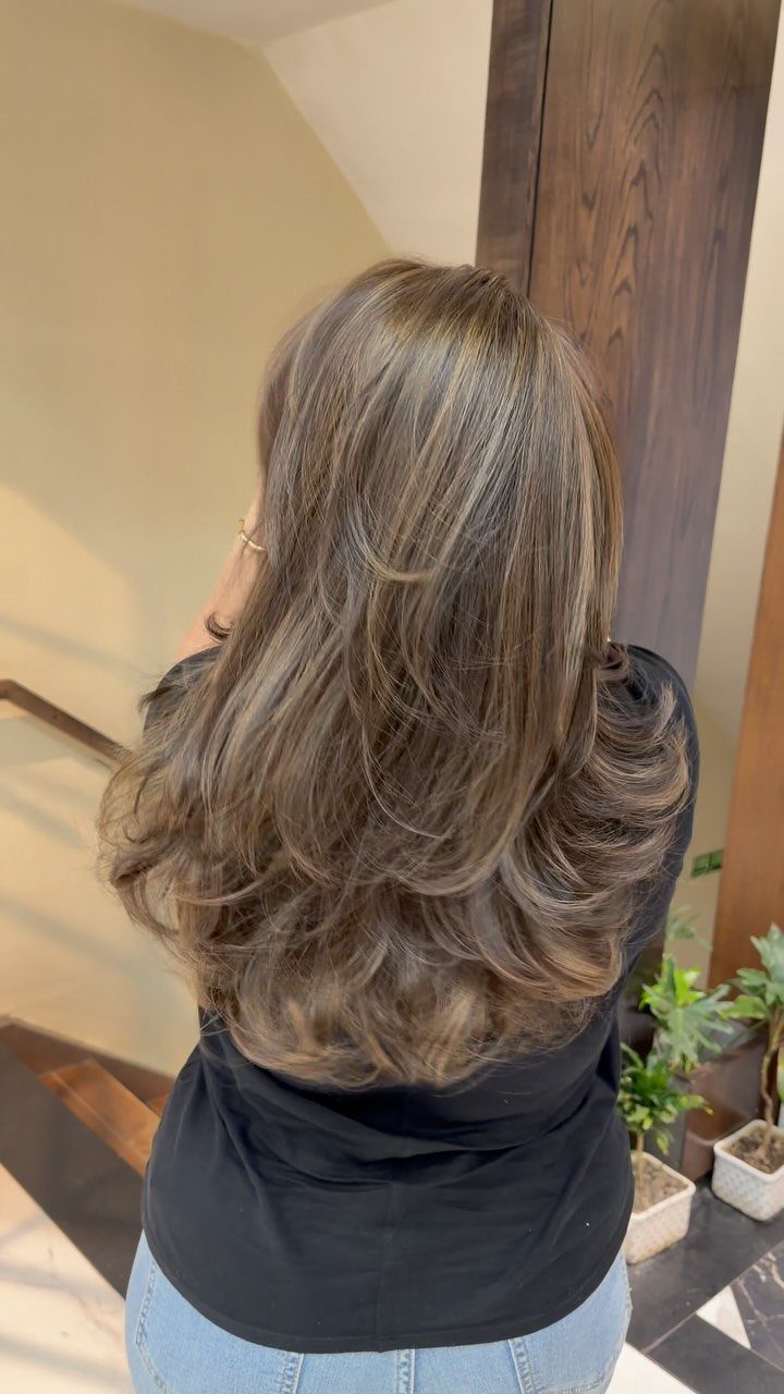 Long layered brown hair with beige blonde highlights styled in voluminous curls.