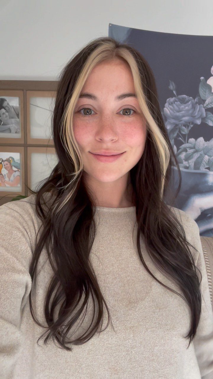 Woman with dark brown hair and chunky blonde face-framing money piece highlights.