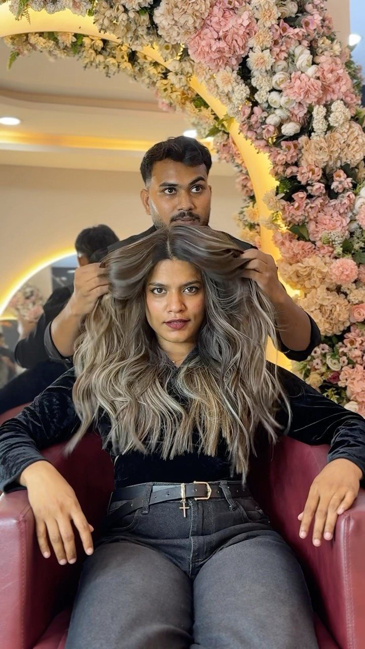 Woman with long wavy ash-blonde highlights and dark roots in a hair salon.