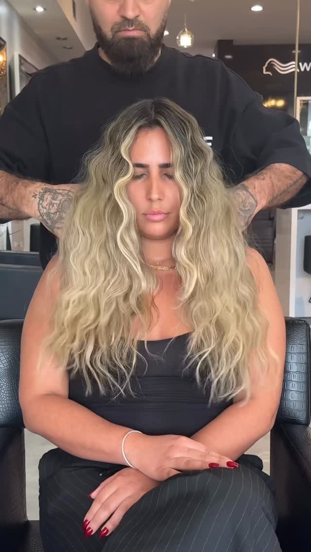Woman with long wavy blonde balayage hair and dark roots in a salon
