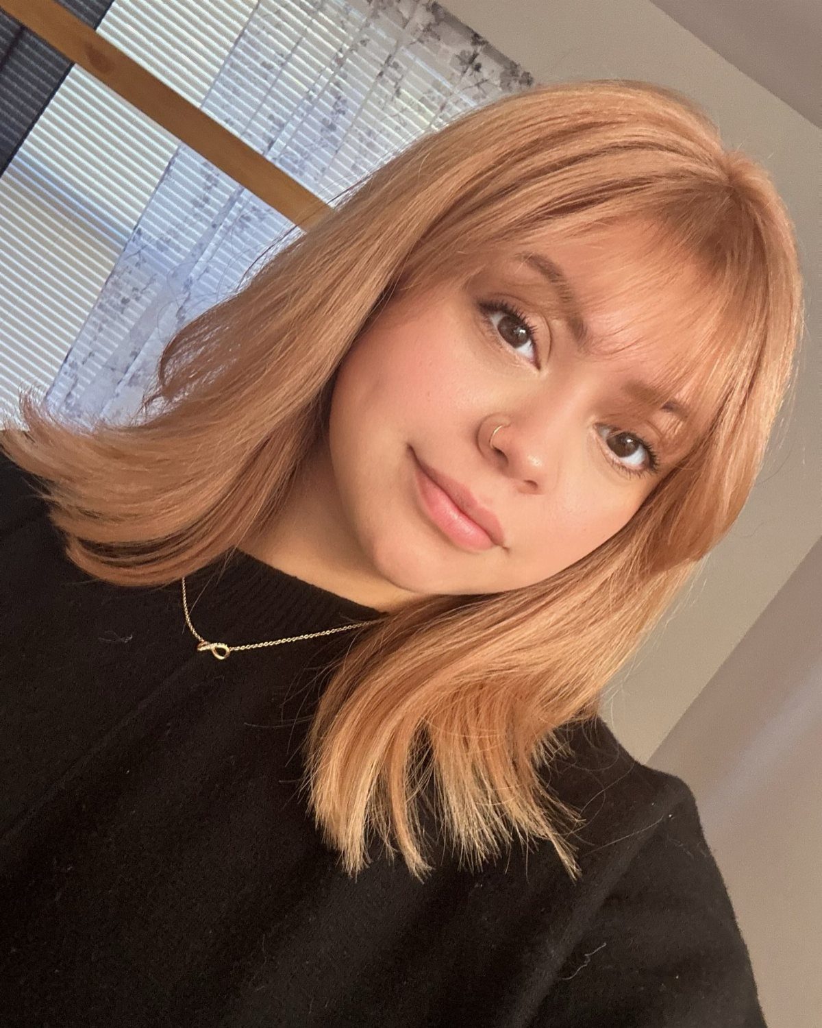 Woman with strawberry blonde hair and bangs wearing a black top and necklace.