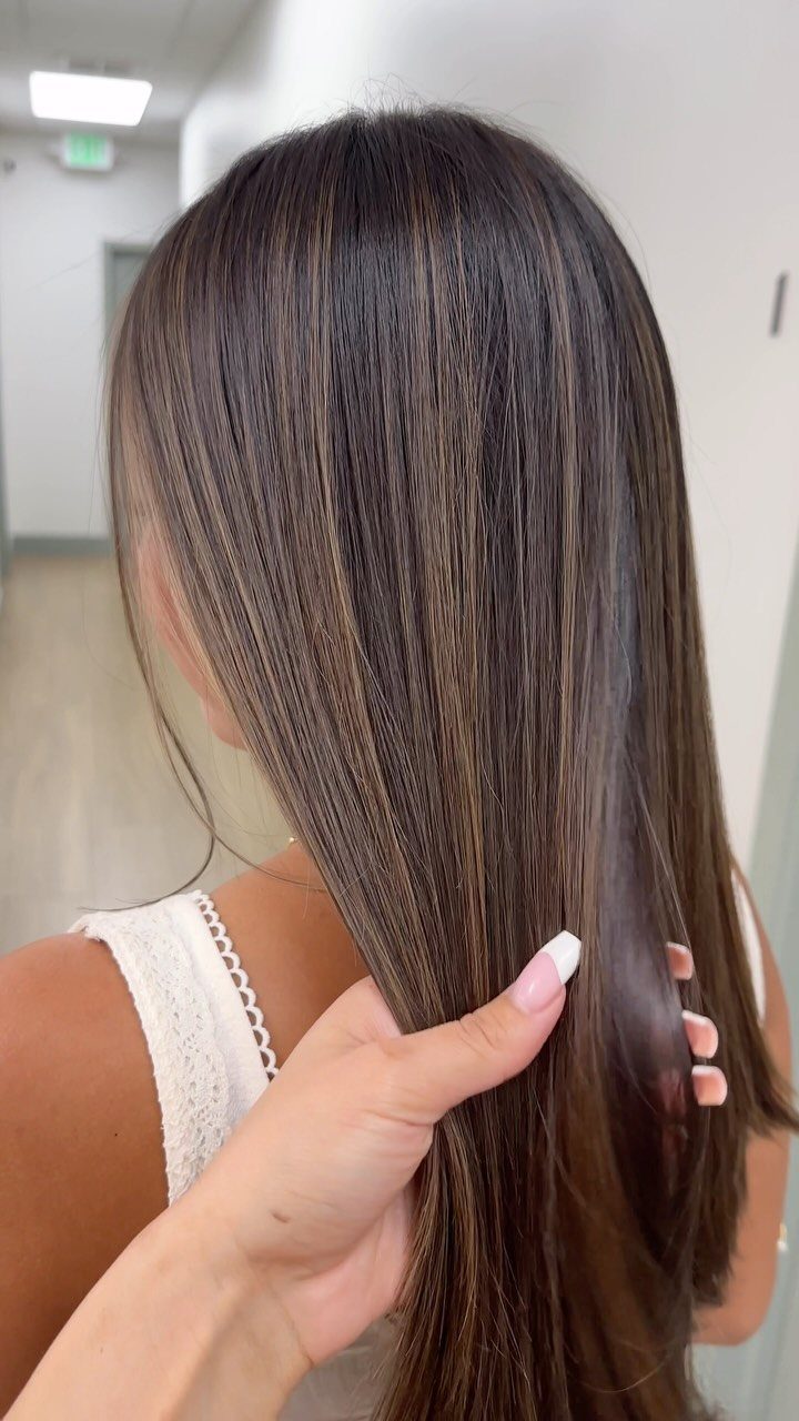 Long chocolate brown hair with thin toffee highlights held by a hand.