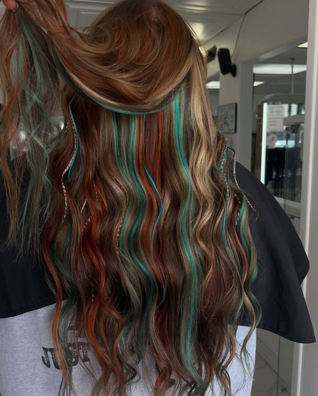Long wavy brown hair with vertical copper and teal blue highlights from behind.