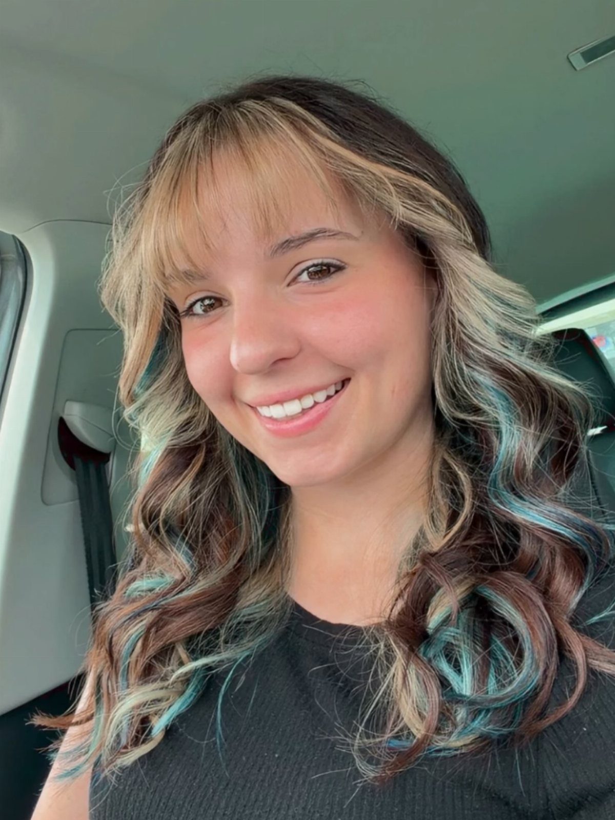 Woman with wavy brown hair featuring scattered blonde, copper, and teal blue streaks.