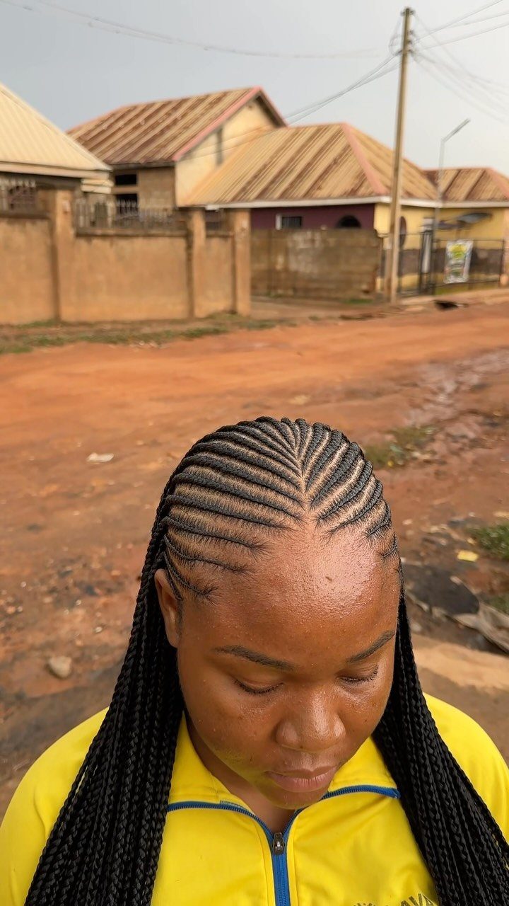 Woman with black cornrow hair styles and long braids wearing a yellow jacket.