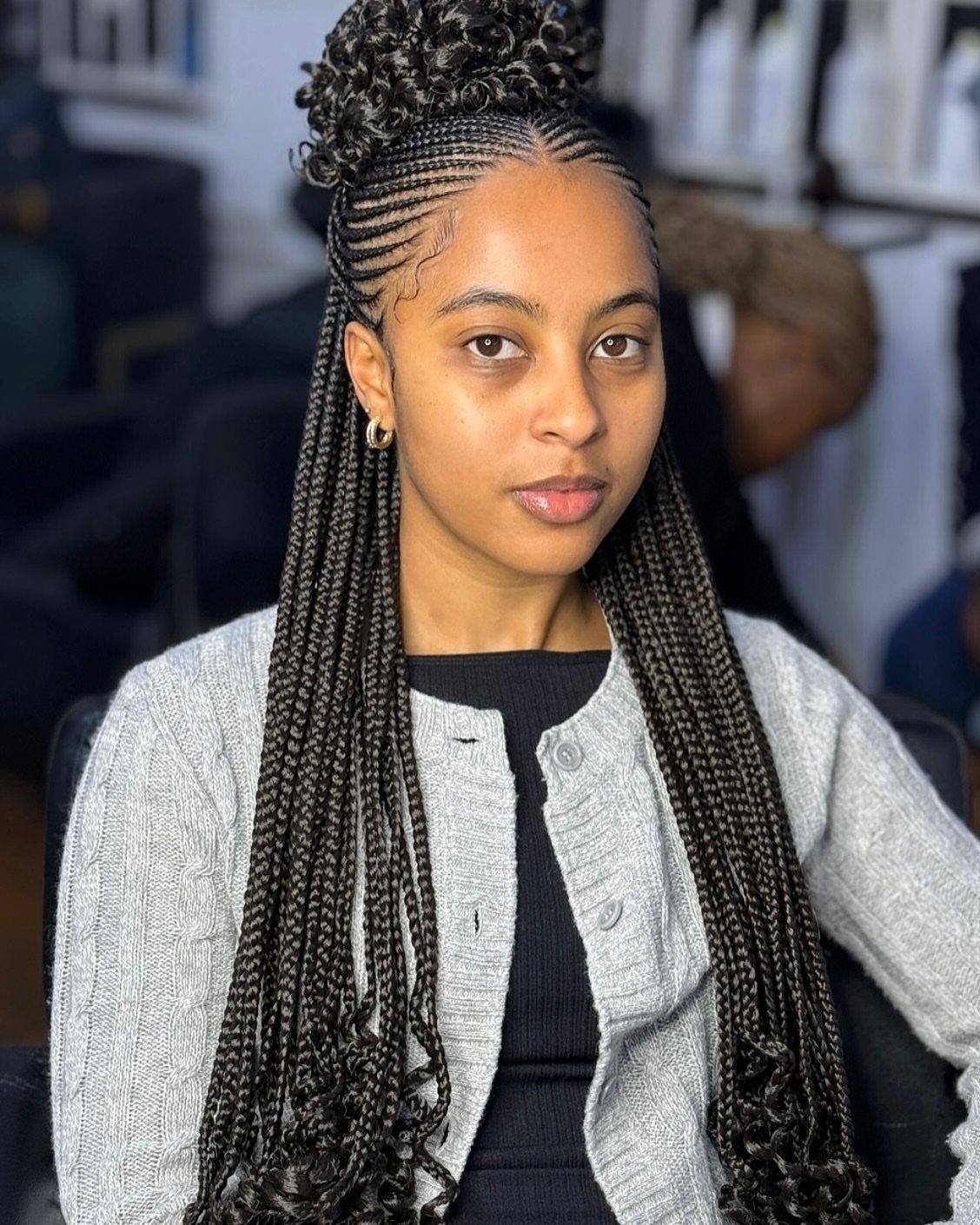 Woman with cornrows styled into a high bun and long curly loose ends.