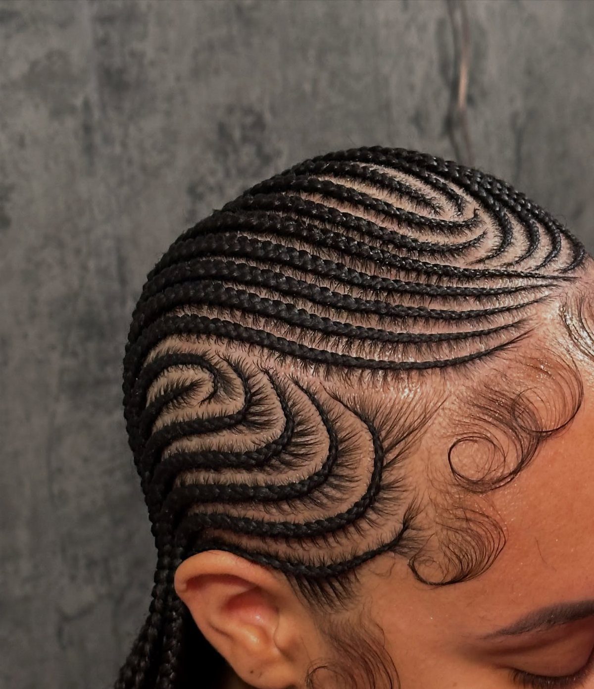 Curved cornrow braids on a person with styled curly edges against grey background