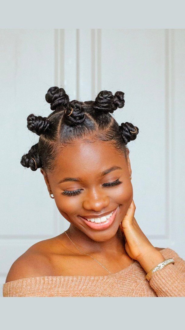 Woman with hair styled in Bantu knots smiling against a white door background