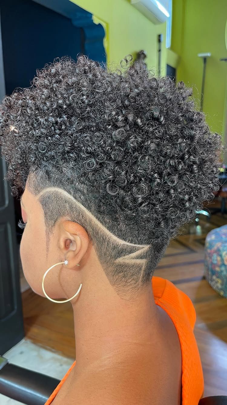 Person with a curly afro and a geometric shaved design on the side.