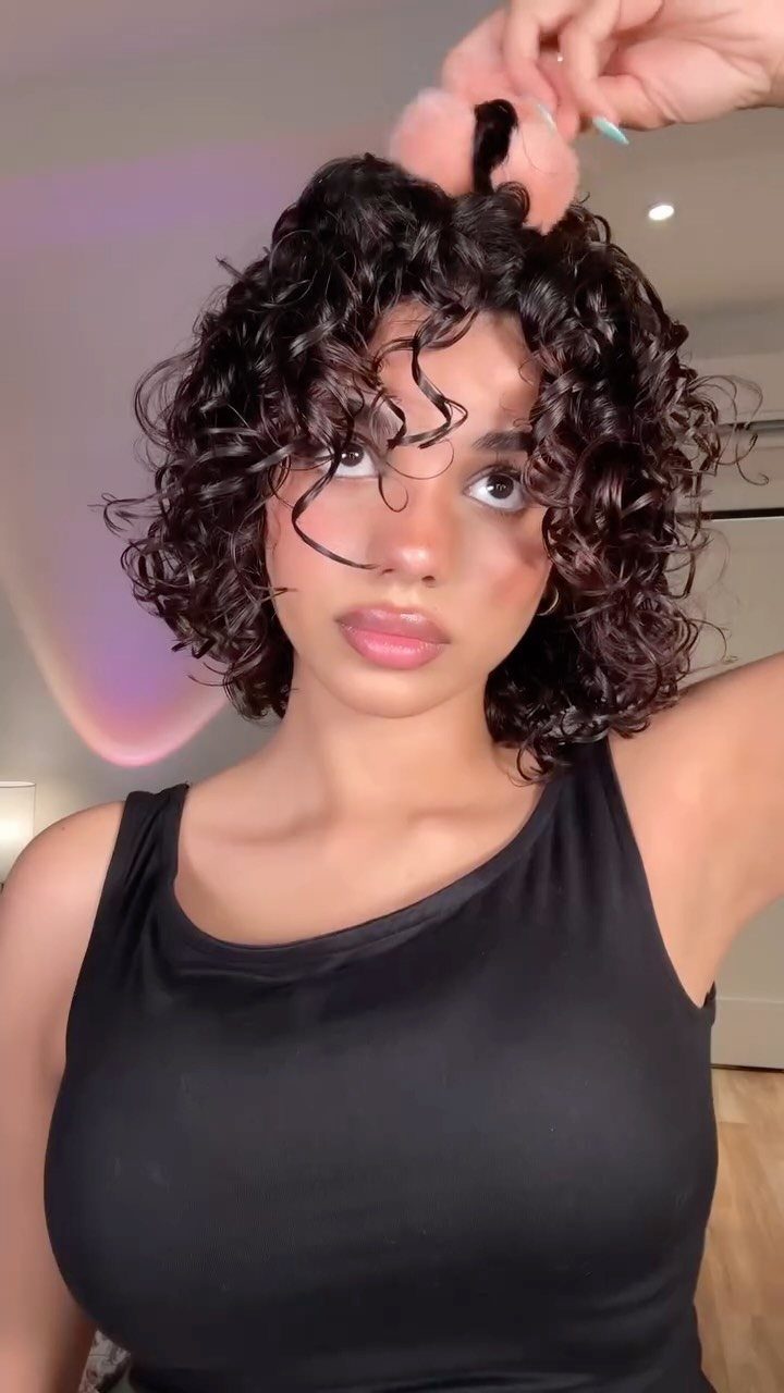 Woman with a curly bob hairstyle and dark hair wearing a black top.