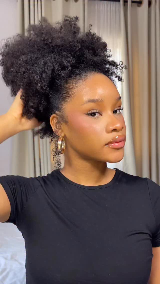 Woman with dark curly hair styled in a high ponytail and gold earrings.