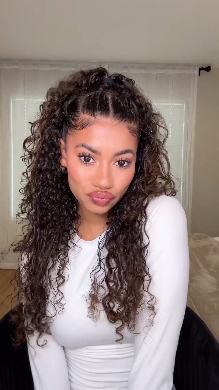 Woman with long dark curly hair in a half-up ponytail wearing white top