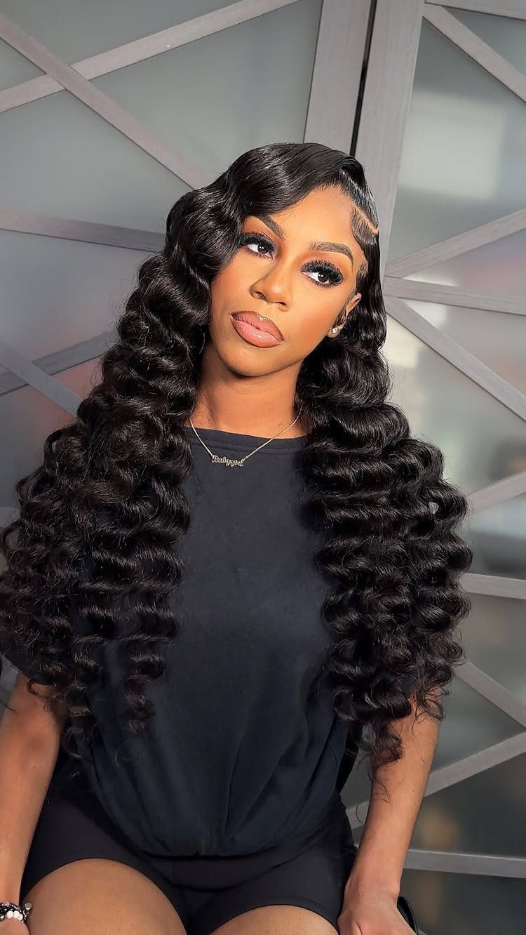 Woman with long, voluminous black loose curls and a side part posing.