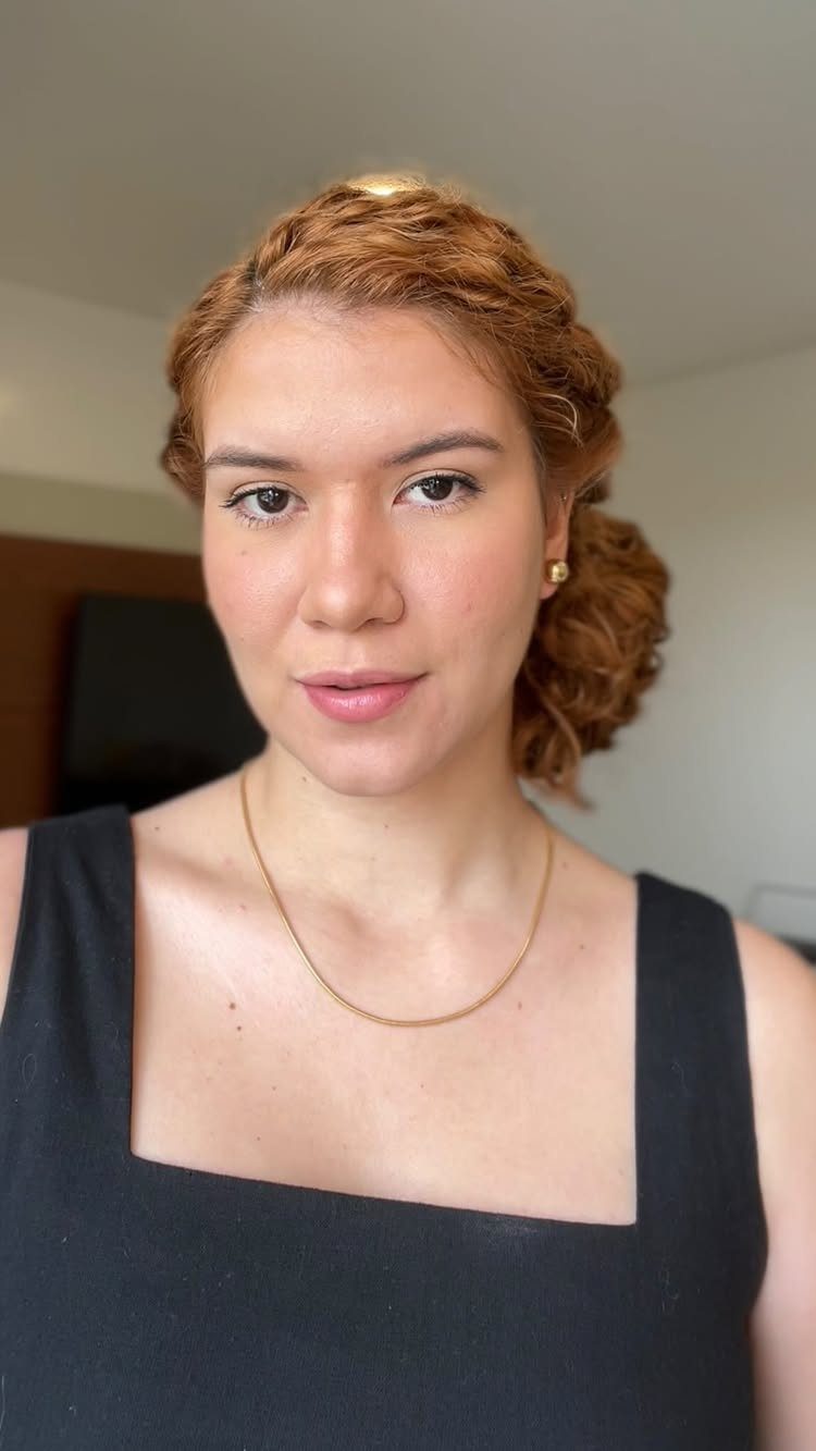 Woman with reddish-brown curly hair styled in a low side curly bun.