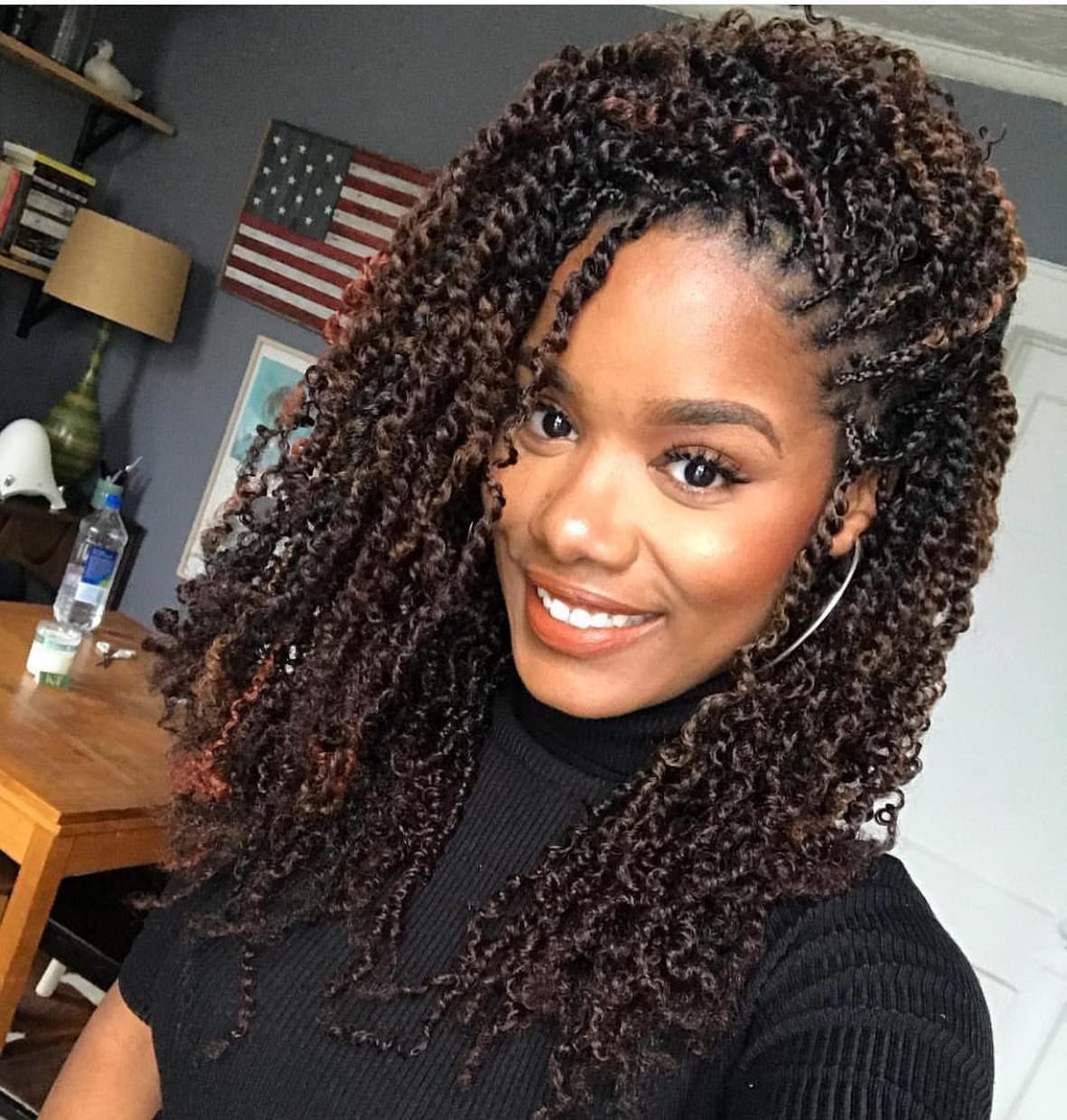 Woman with voluminous dark brown twisted curls and reddish highlights wearing a black turtleneck.