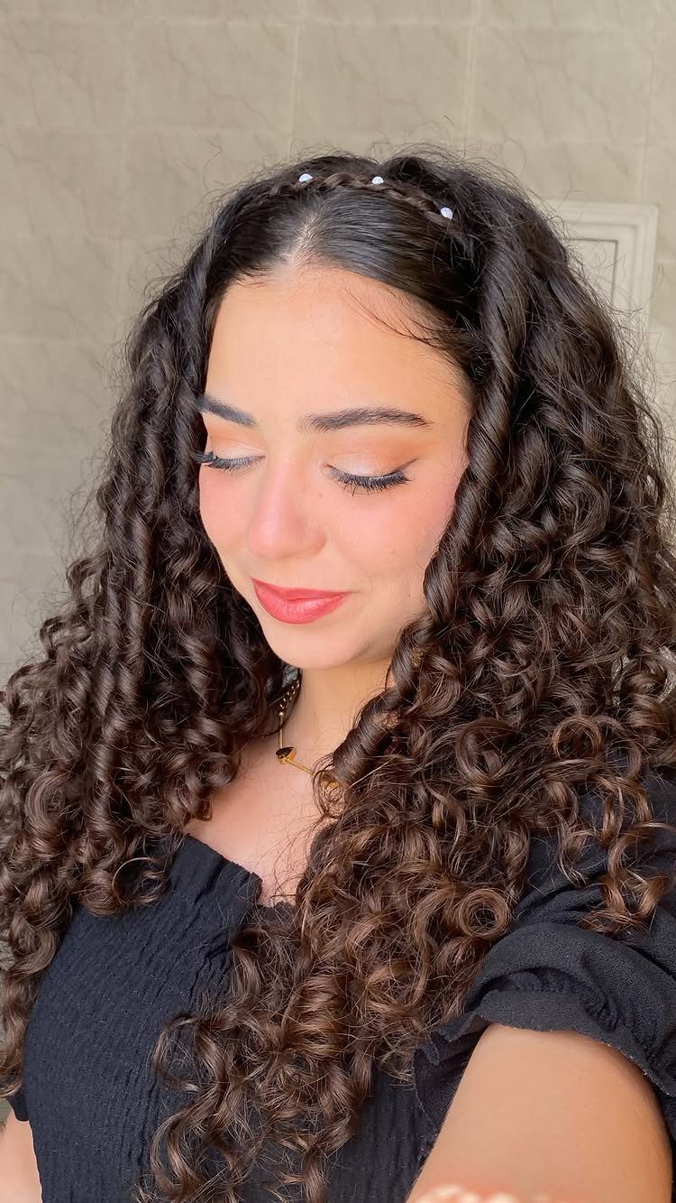 Woman with long brown curls and a pearl-accented braided headband hairstyle.