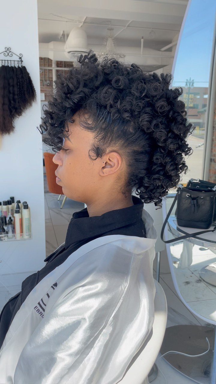 Person with dark curly hair styled in a voluminous faux hawk updo.