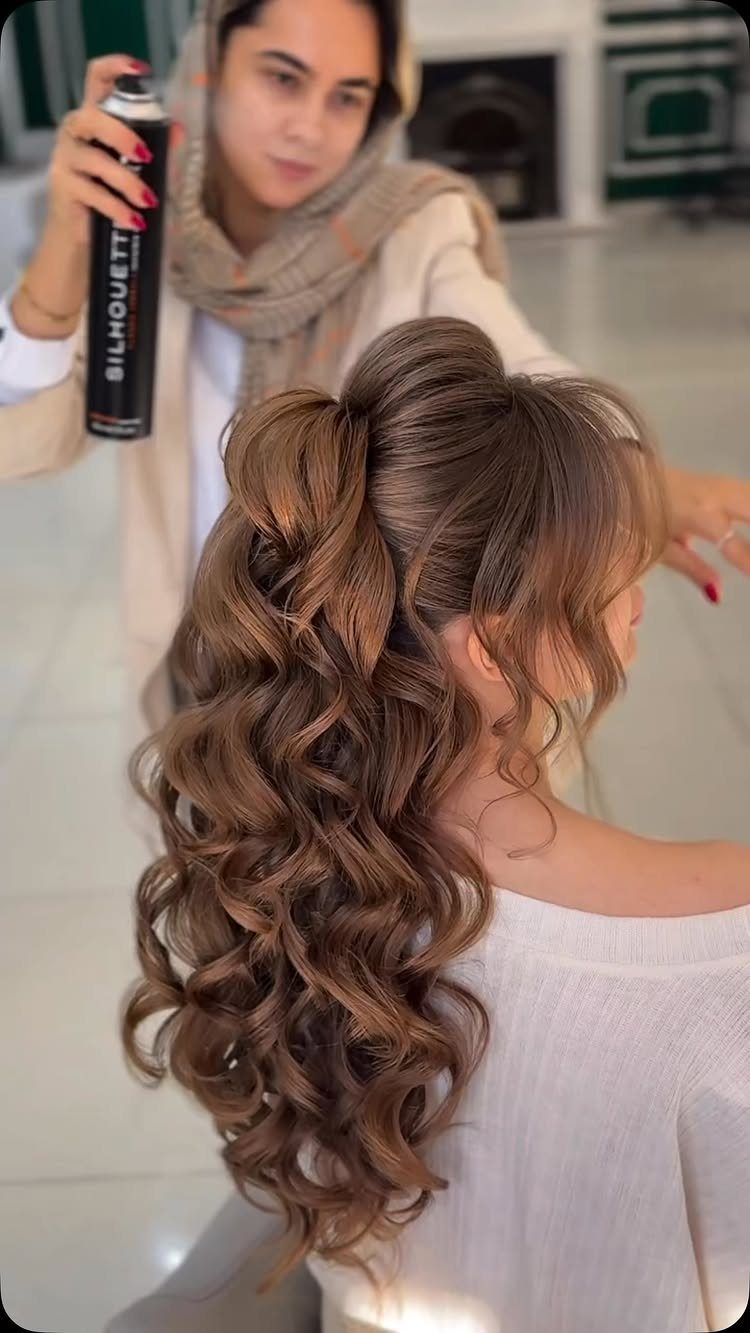 Voluminous brown curly ponytail being styled with hairspray by a professional stylist.