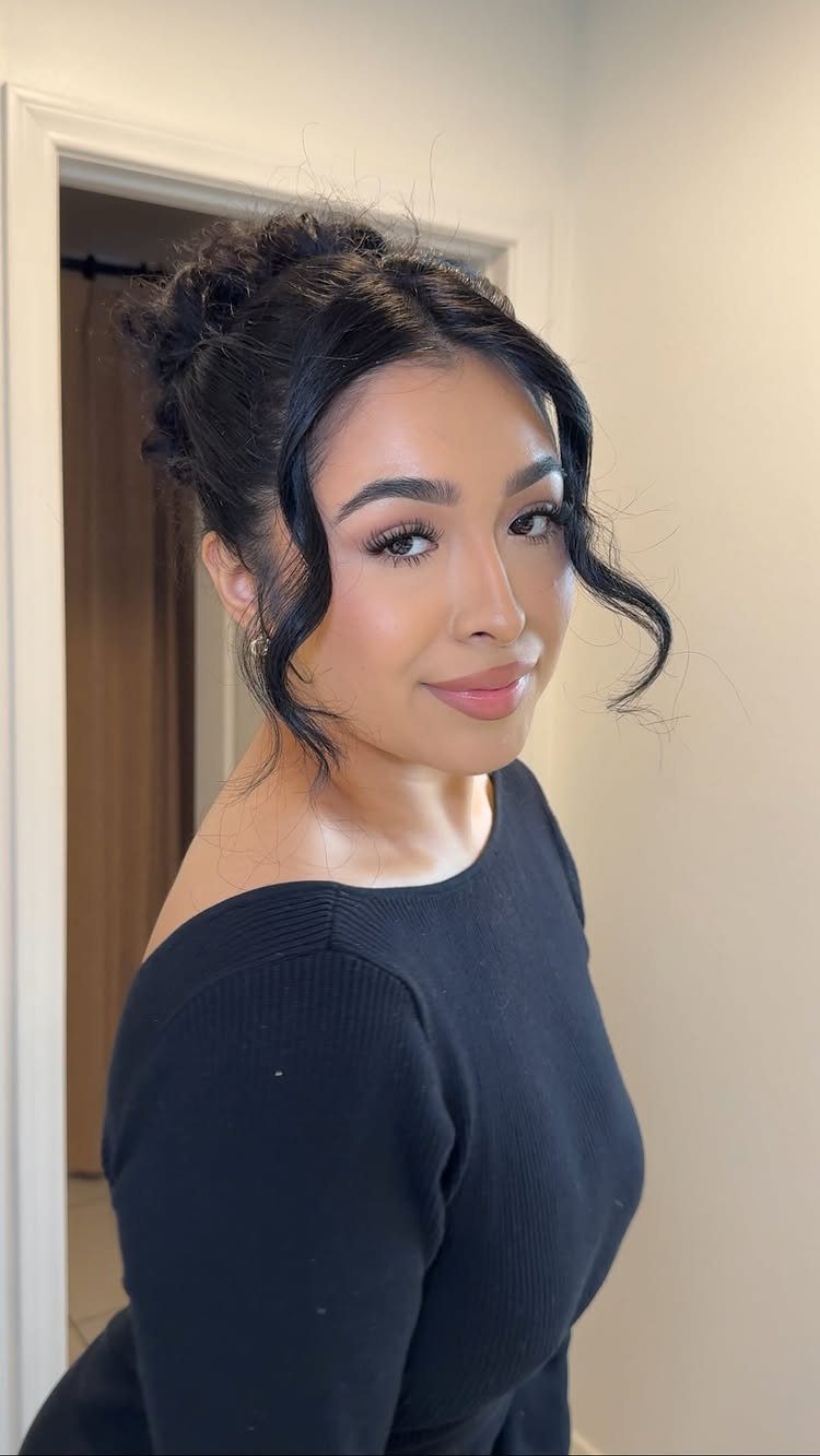 Woman with a messy curly updo and loose tendrils wearing a black top.