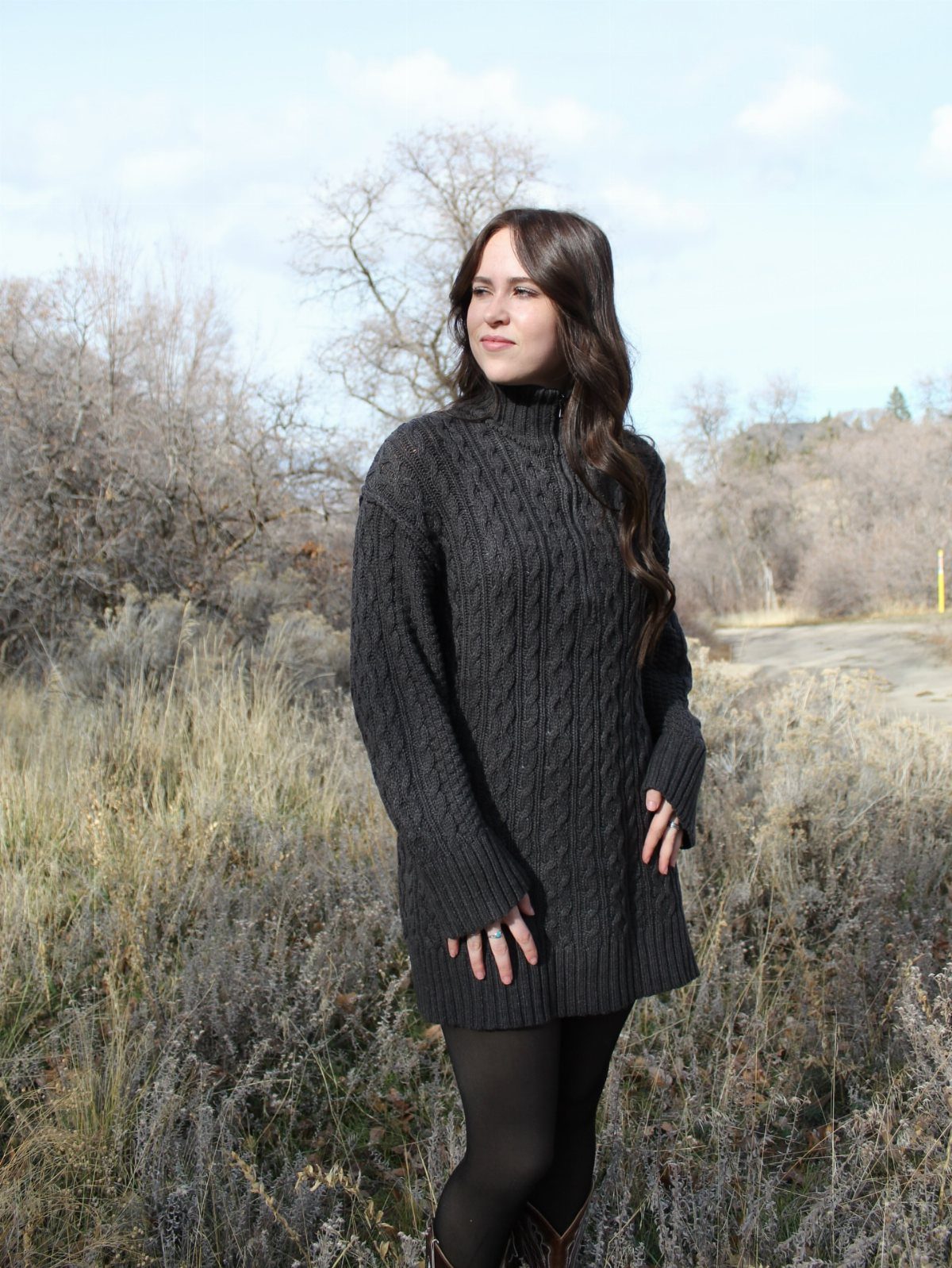 Cute Bonfire Outfits: 11 Ideas for Cozy Fall Nights 11 Woman wearing a grey cable-knit sweater dress and black tights in a field.