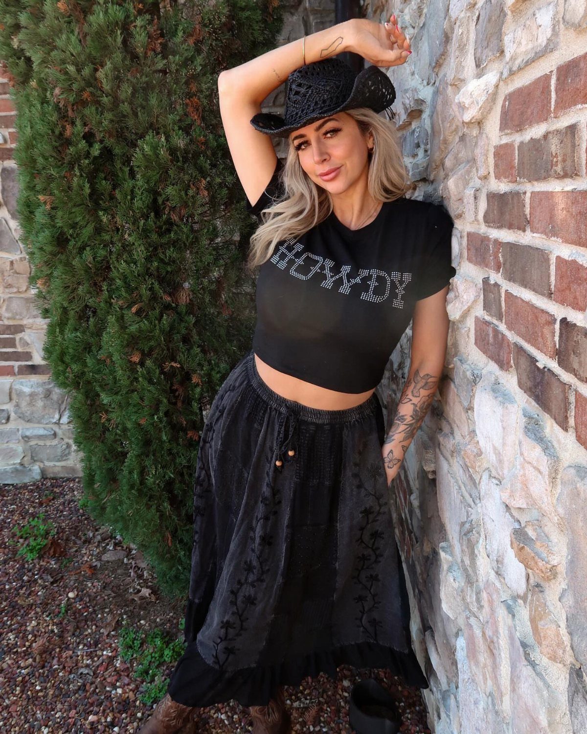 Cute Bonfire Outfits: 11 Ideas for Cozy Fall Nights 10 Woman wearing a black cowboy hat, cropped howdy shirt, and long velvet skirt.