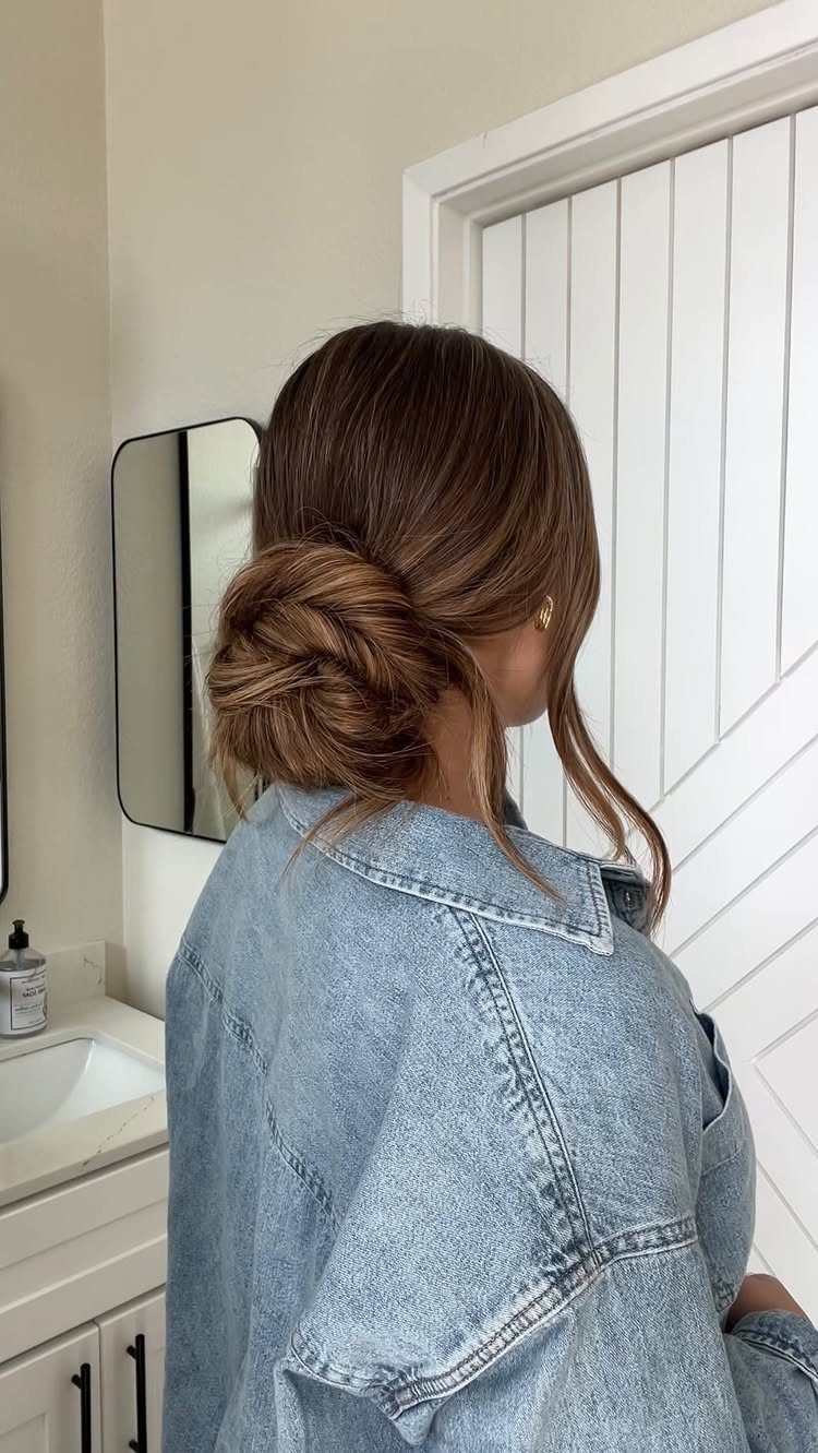 Woman with brown hair styled in a low bun wearing a denim jacket.