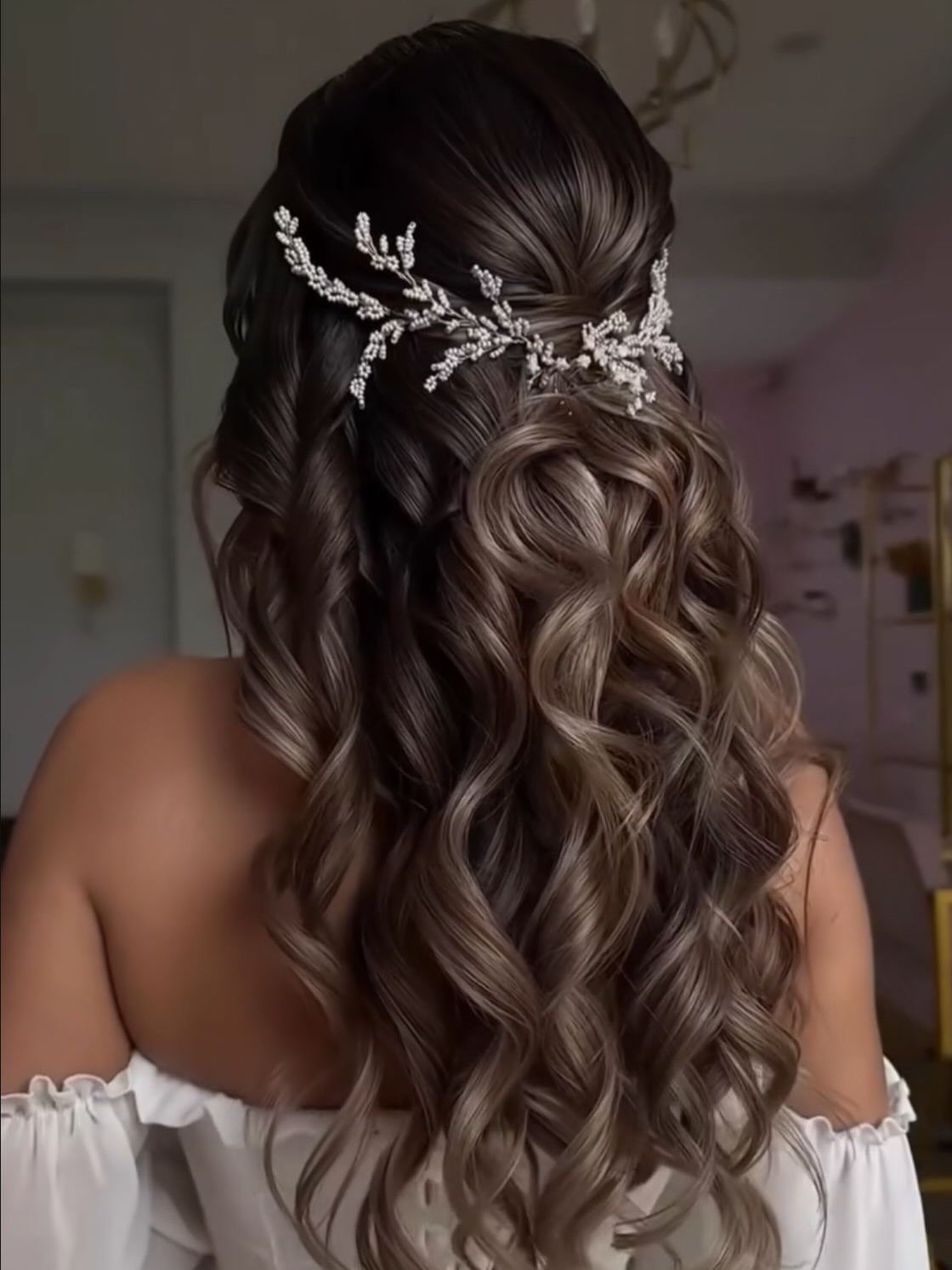 Long wavy brown hair in a half-up style with a silver floral accessory