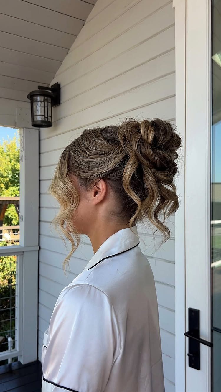 Woman with a blonde messy updo and loose curls wearing a white robe.