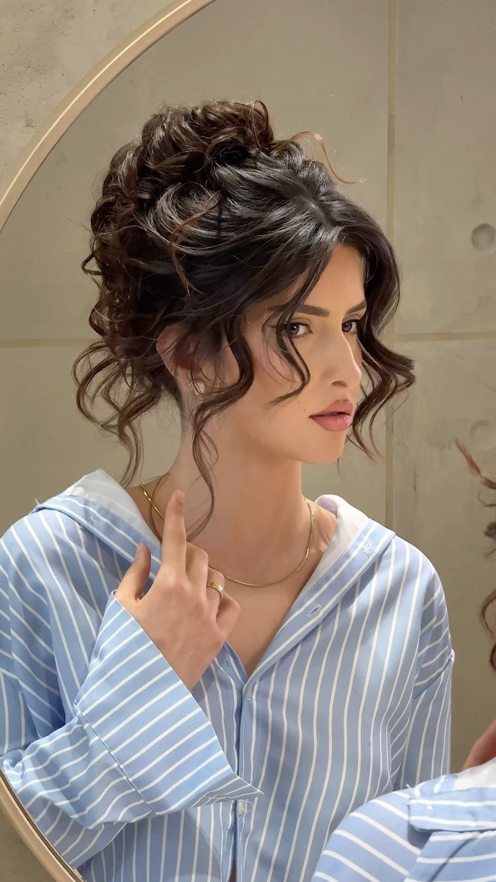 Woman with a romantic curly updo and loose tendrils wearing striped blue pajamas.