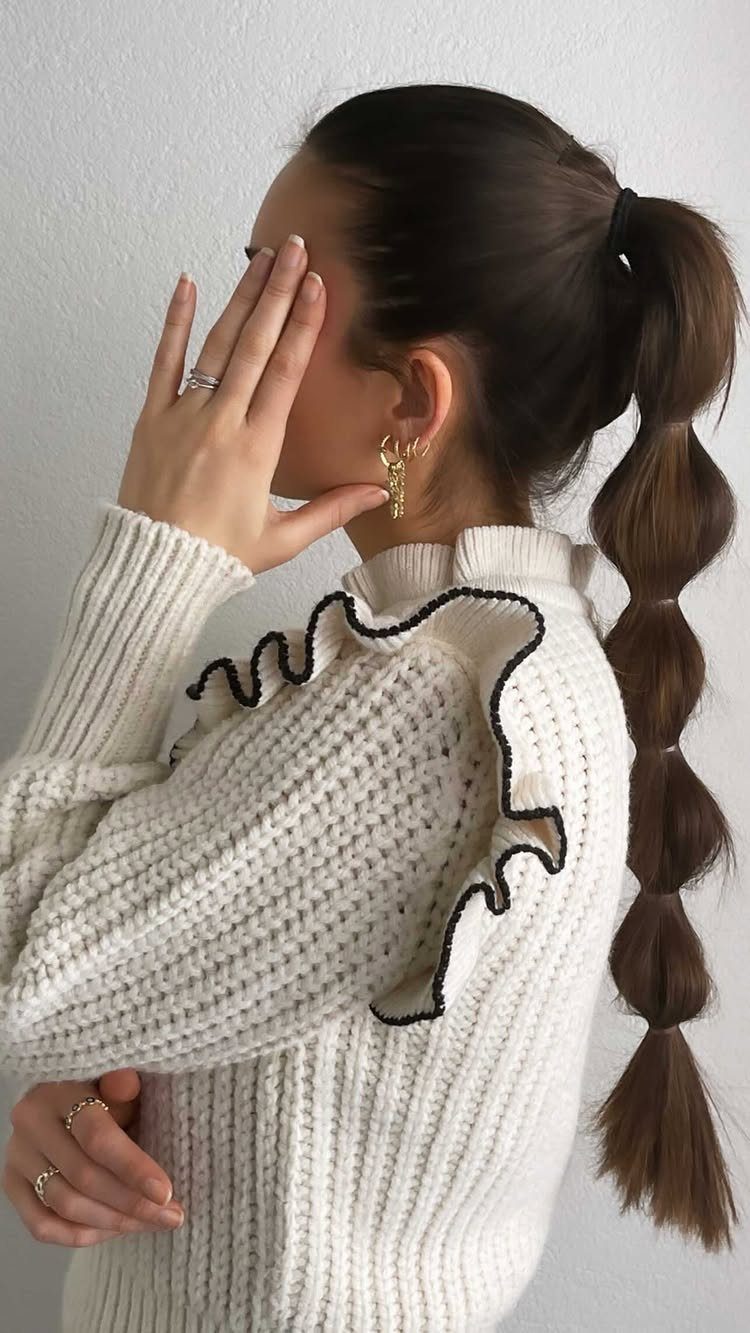 Woman with brown hair in a bubble ponytail wearing a white ruffled sweater.