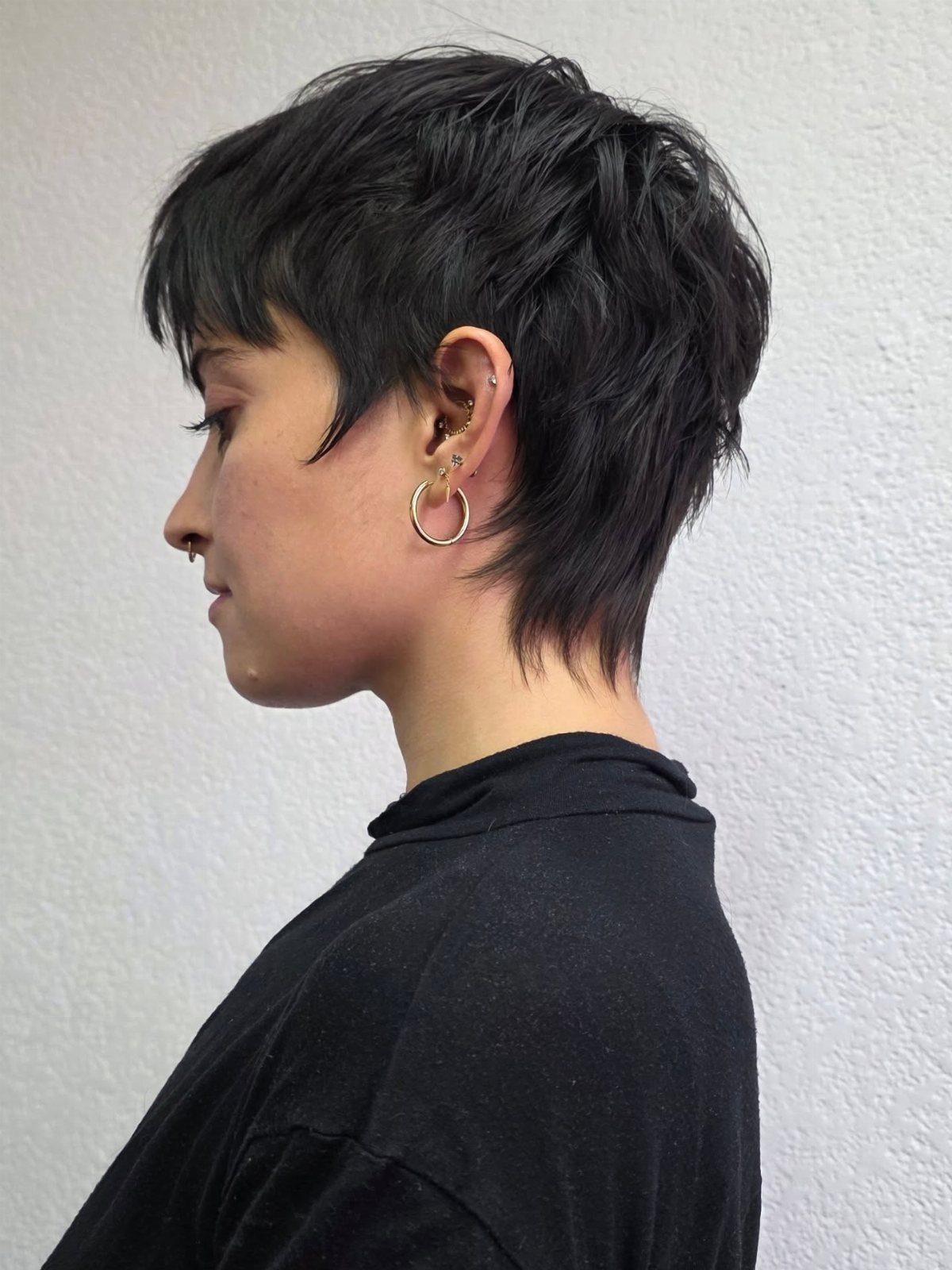 Person with a dark feathered pixie cut and gold hoop earrings in profile.