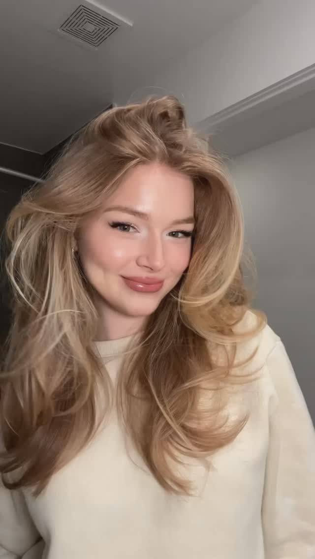Woman with voluminous blonde hair styled in a fluffy blowout wearing a cream sweater.