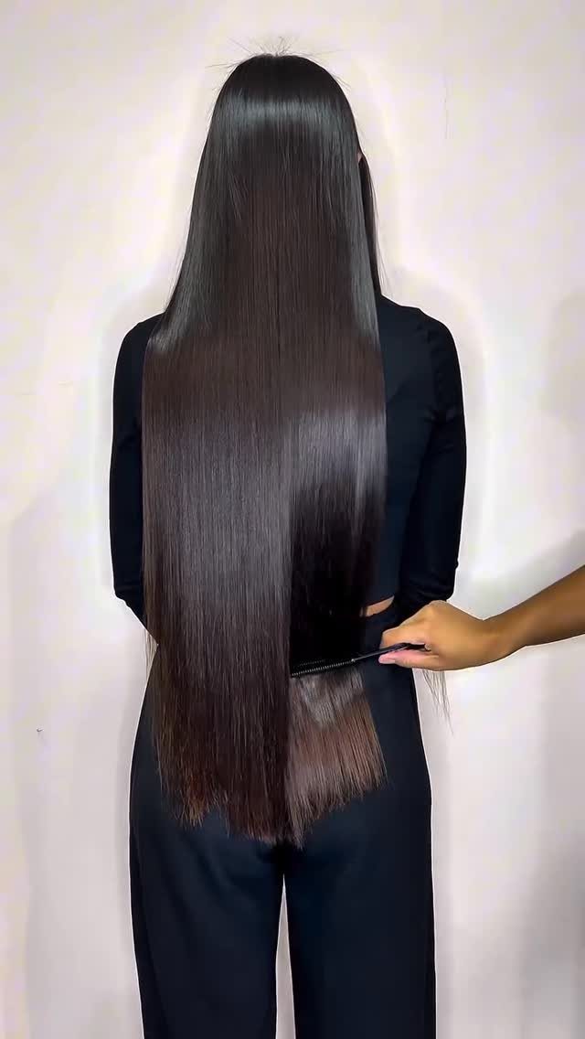Long, sleek, shiny dark brown straight hair viewed from behind against a light wall.