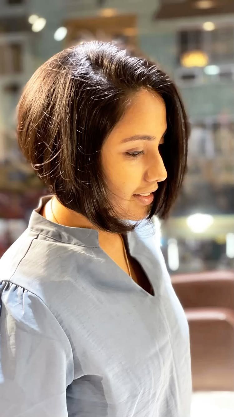 Woman with a dark brown graduated chin-length bob haircut wearing a blue blouse.