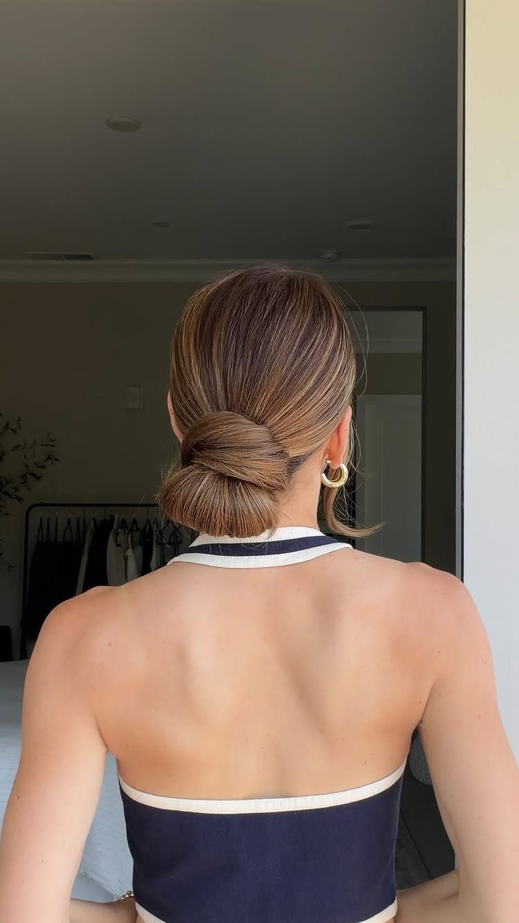 Woman with brown straight hair styled in a low twisted bun from behind.