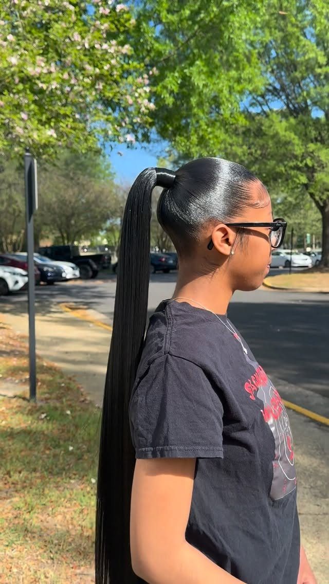 Person with long straight black hair in a high slicked-back ponytail outdoors.
