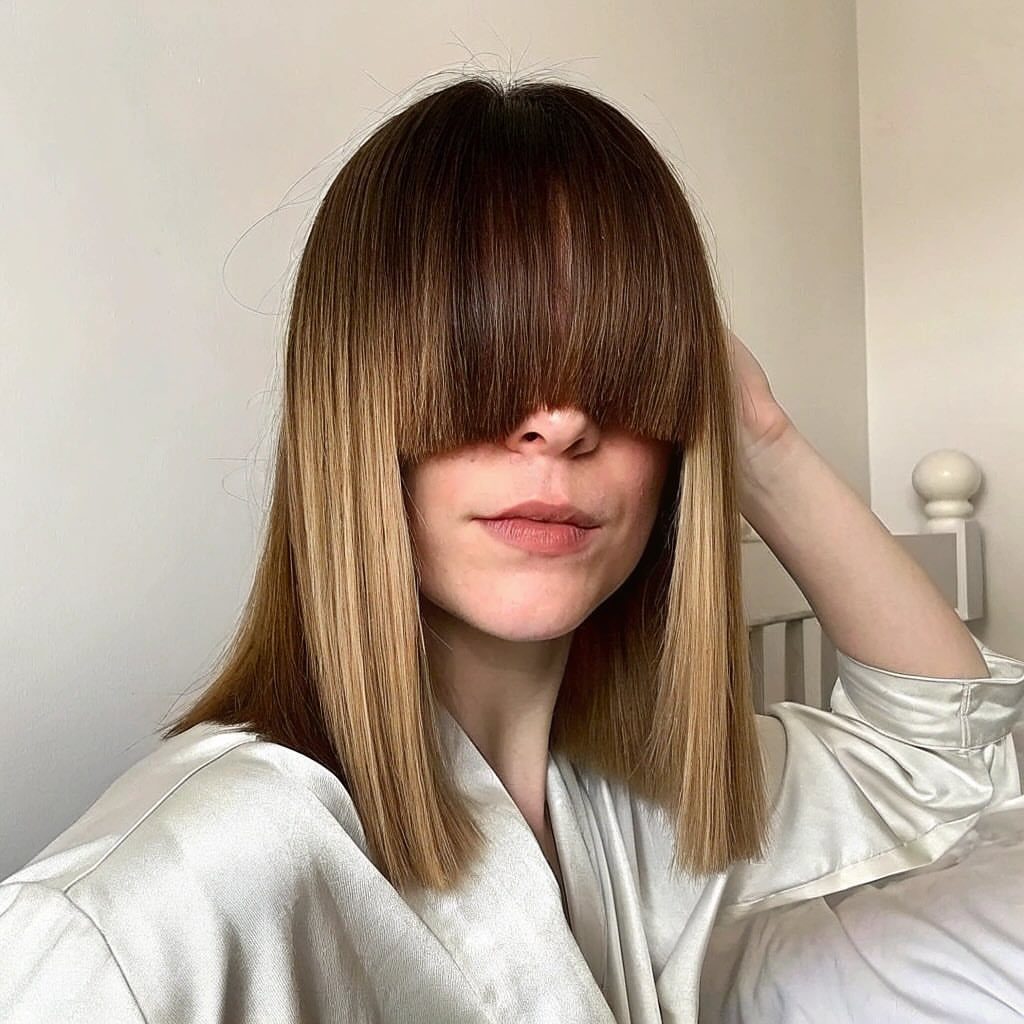 Woman with straight brown hair and long straight-across bangs covering her eyes.