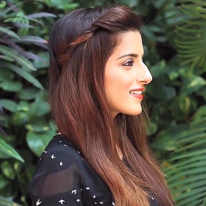 Woman with long brown hair and a small side braid against green leaves