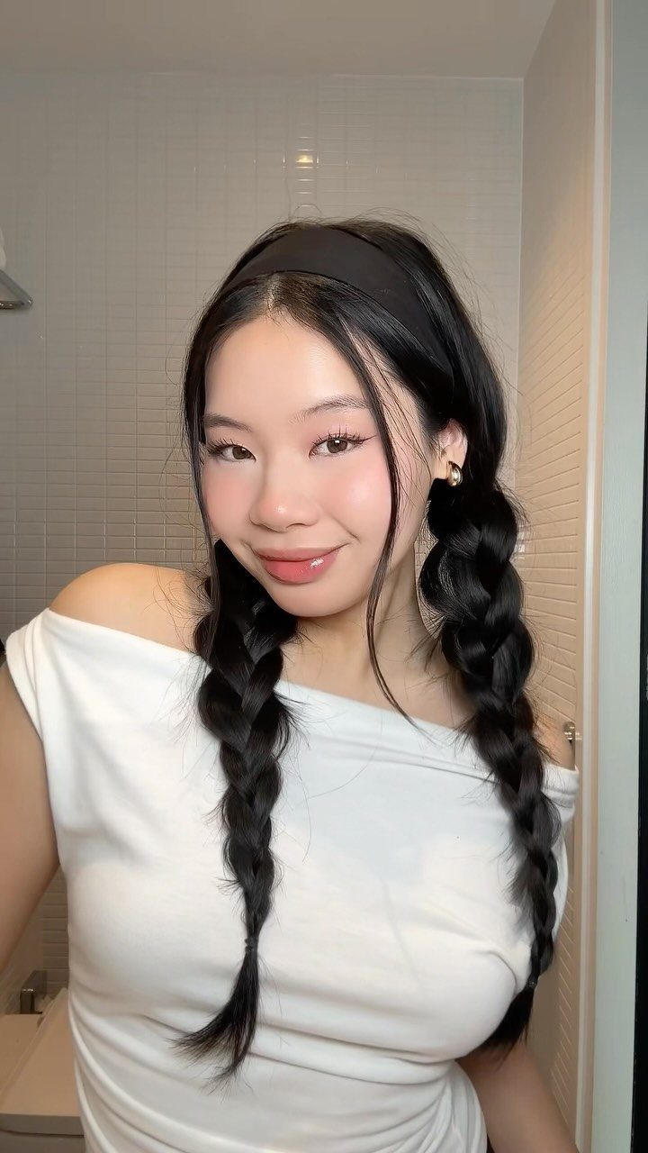 Woman with black hair in two braided pigtails wearing a white off-shoulder top.