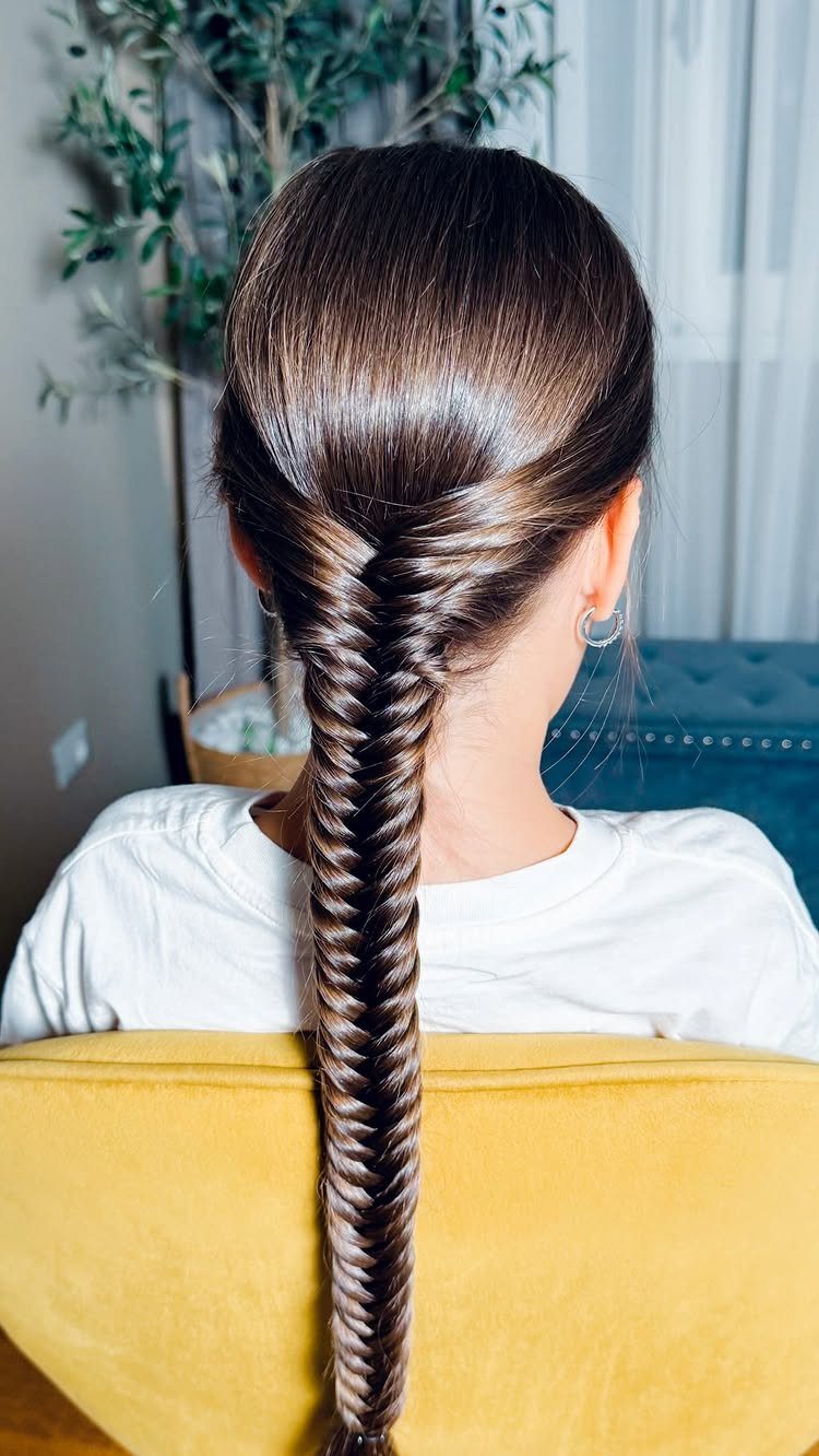 Long brown hair styled in a tight fishtail braid on a person's back