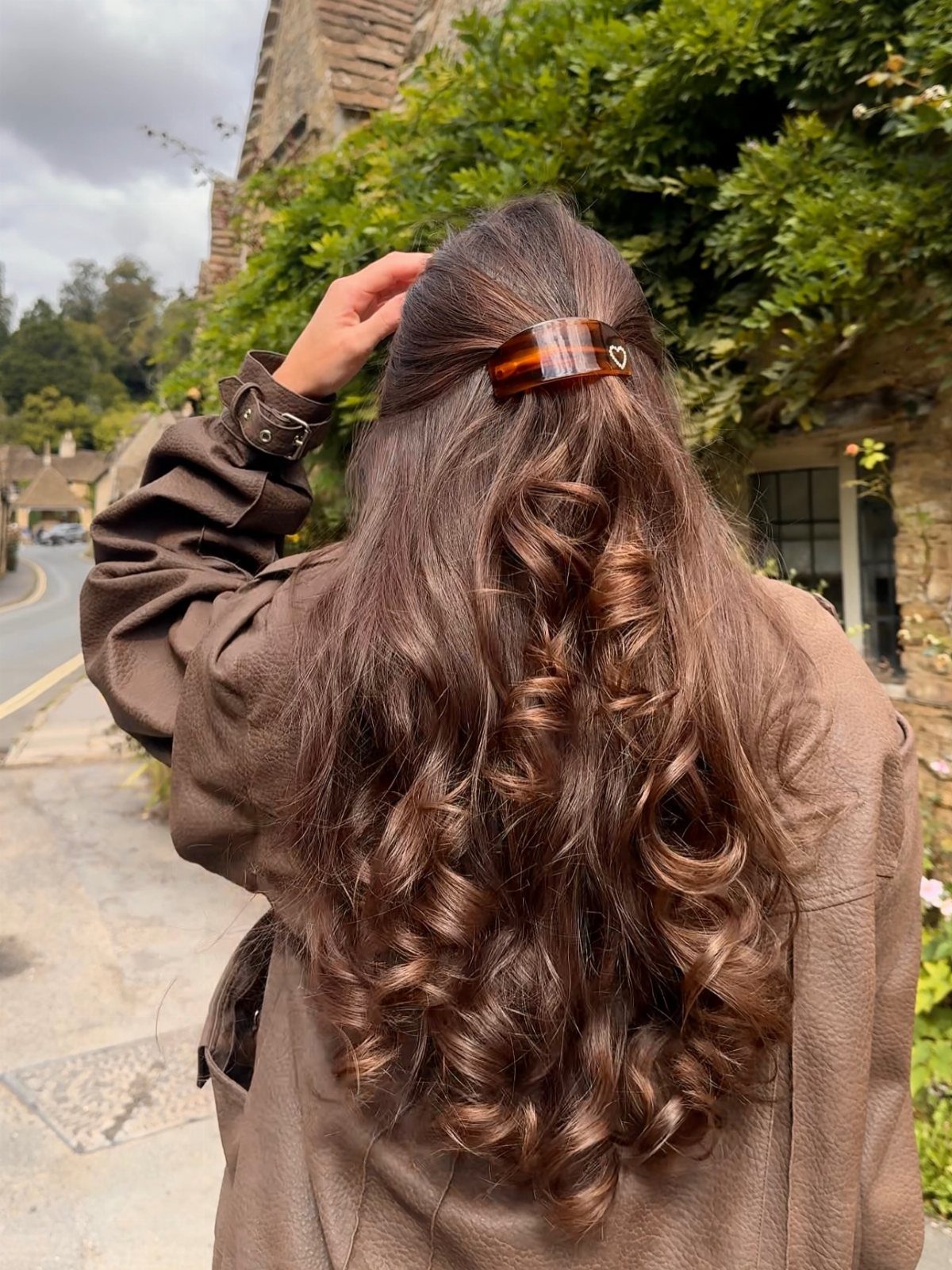 Long curly brown hair styled half-up with a tortoiseshell claw clip outdoors.