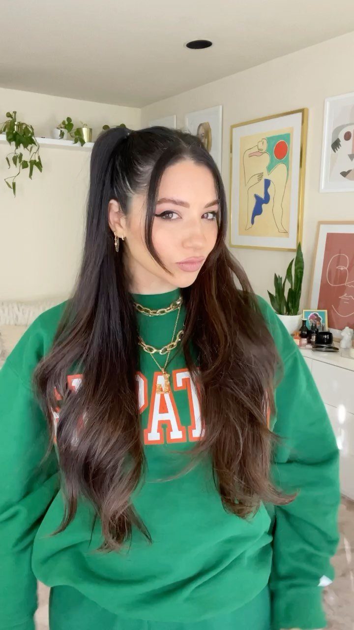 Woman with long brown hair in a half-up high ponytail wearing green sweatshirt