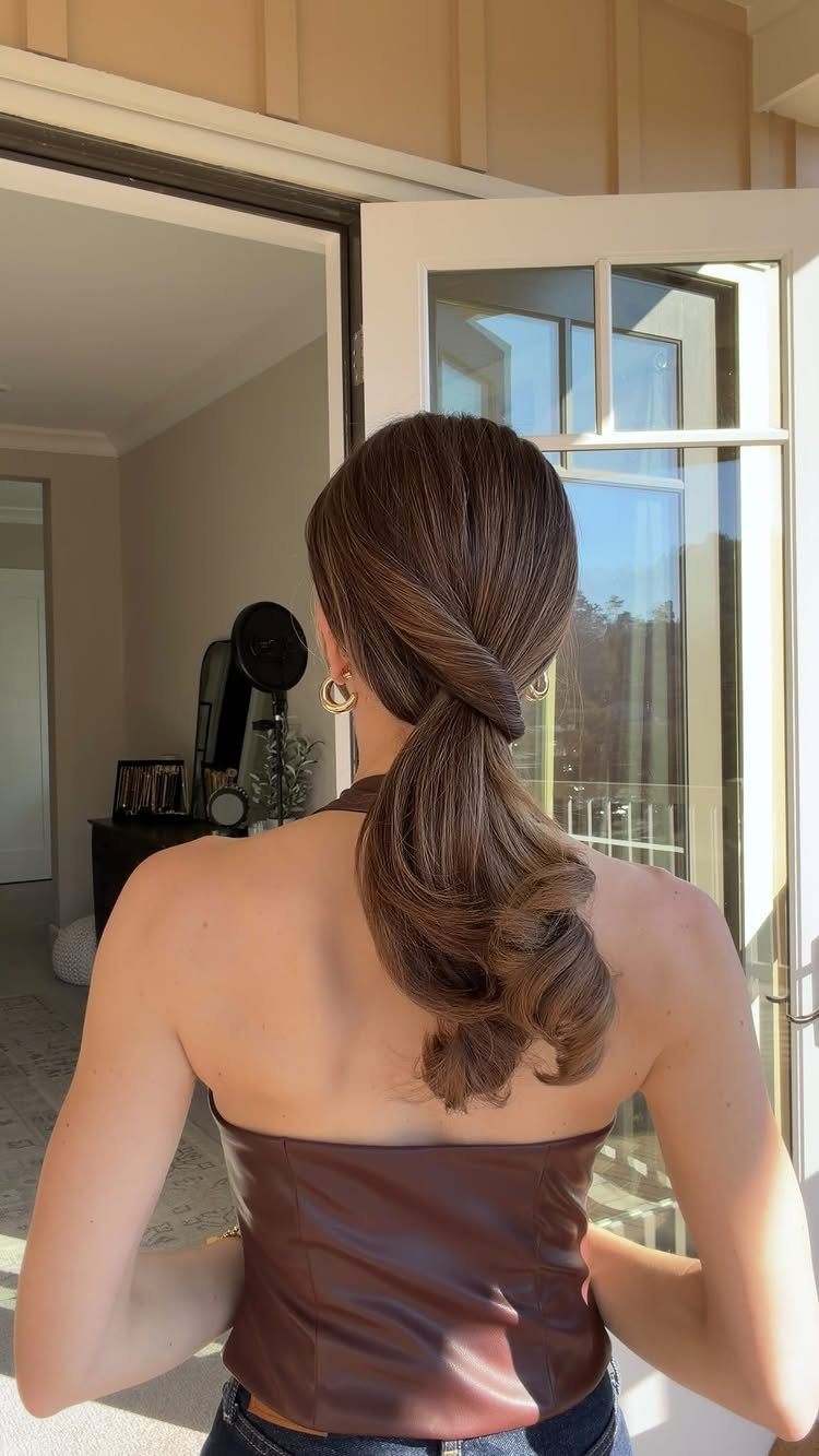 Woman with brown hair styled in a low twisted ponytail wearing leather top