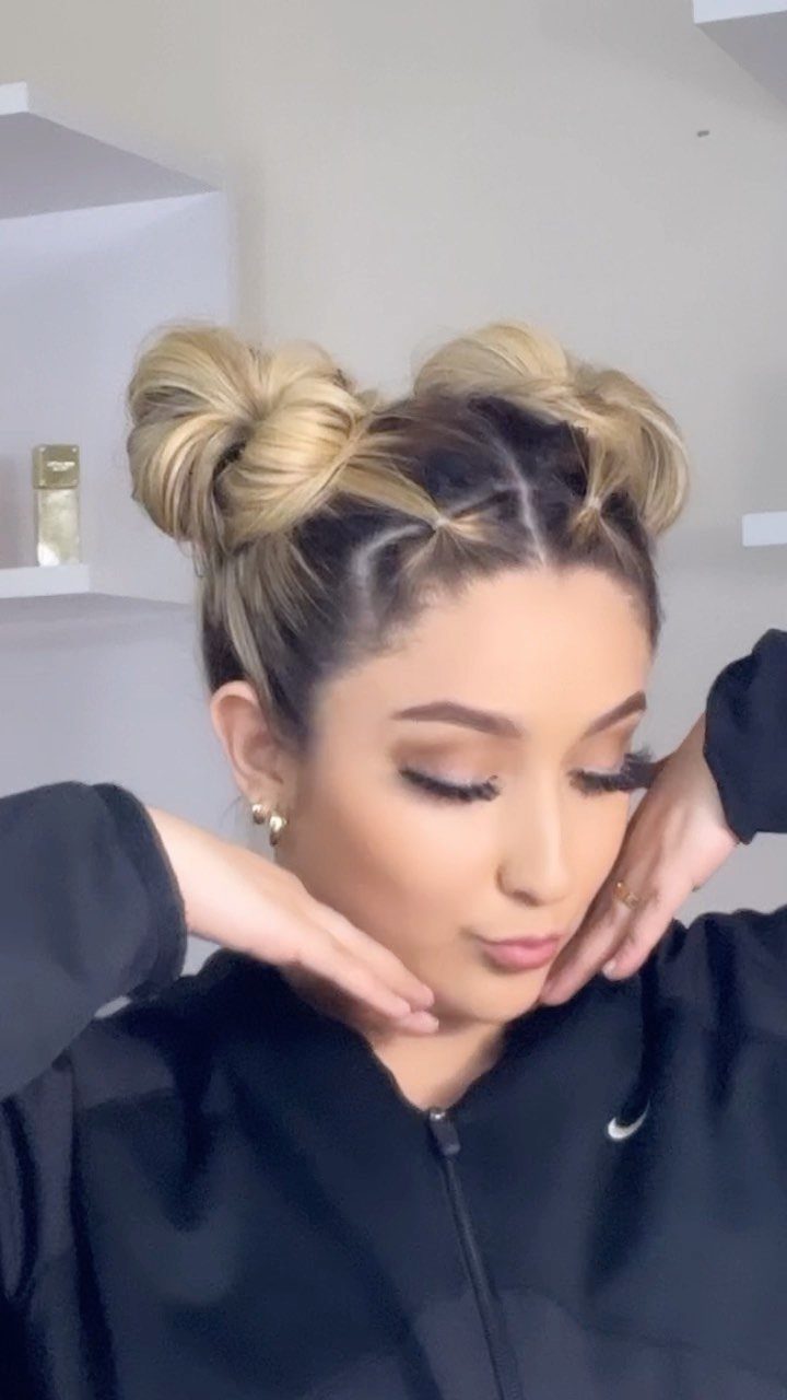 Woman with blonde hair styled in two high space buns wearing black jacket.